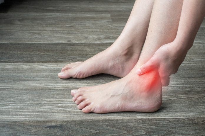 Close-up of woman hands holding and touching her ankle, suffering from ankle pain.