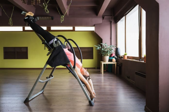 A woman doing inversion therapy hanging upside down on an inversion table, the therapy session is being done in a studio