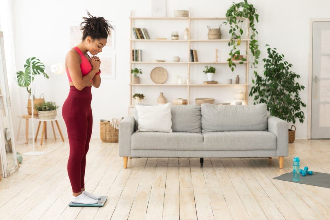 Happy Black Girl Weighing Herself On Weight-Scales Losing Weight Indoor 11860 Vista Del Sol, Ste. 128 Holiday Weight Gain, Back Pain, and Chiropractic Recommendations