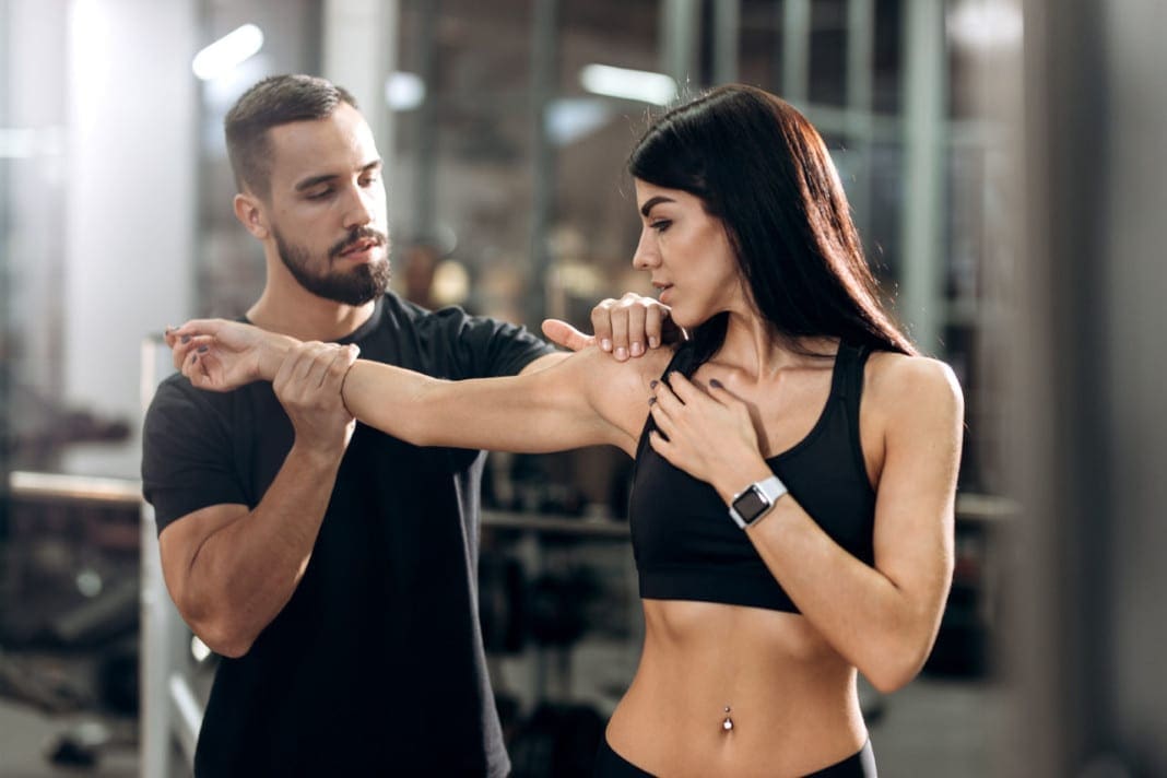 Fitness coach explans to athletic girl dressed in black sport clothes how works muscles of the arms