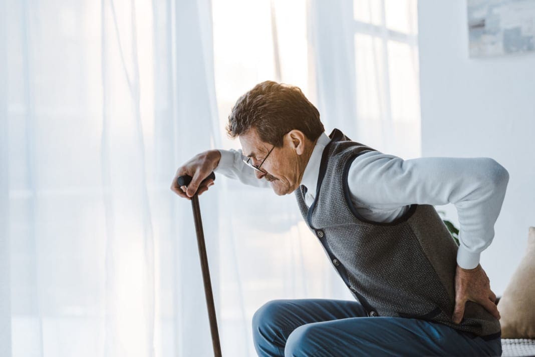 senior man with walking cane holding back while standing up from