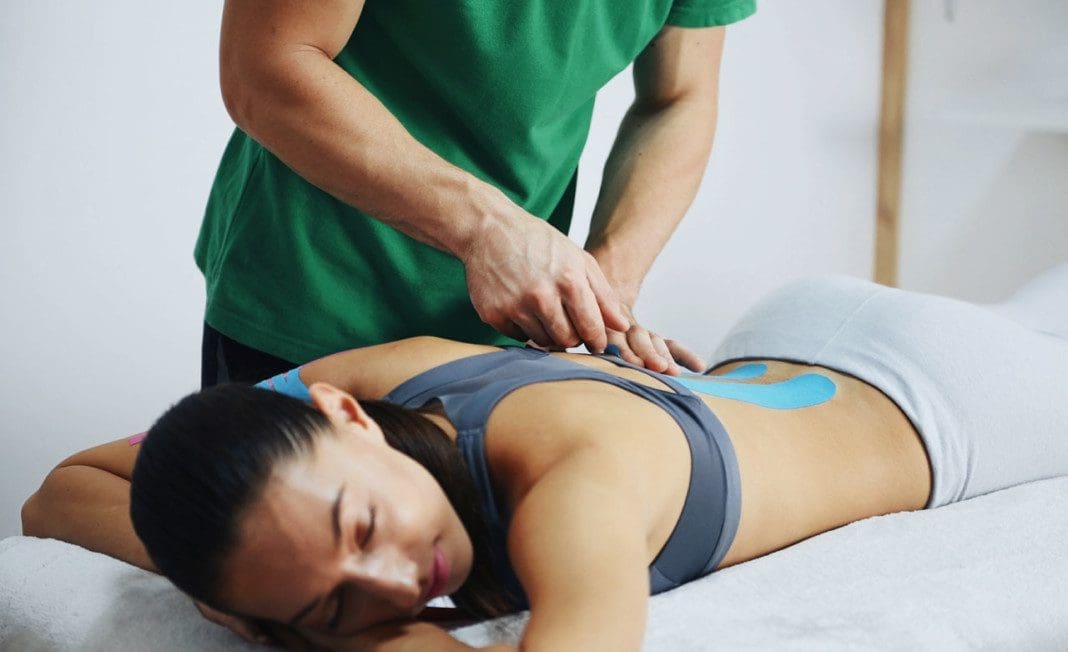 Doctor helps woman by shoulder treatment with kinesio tape