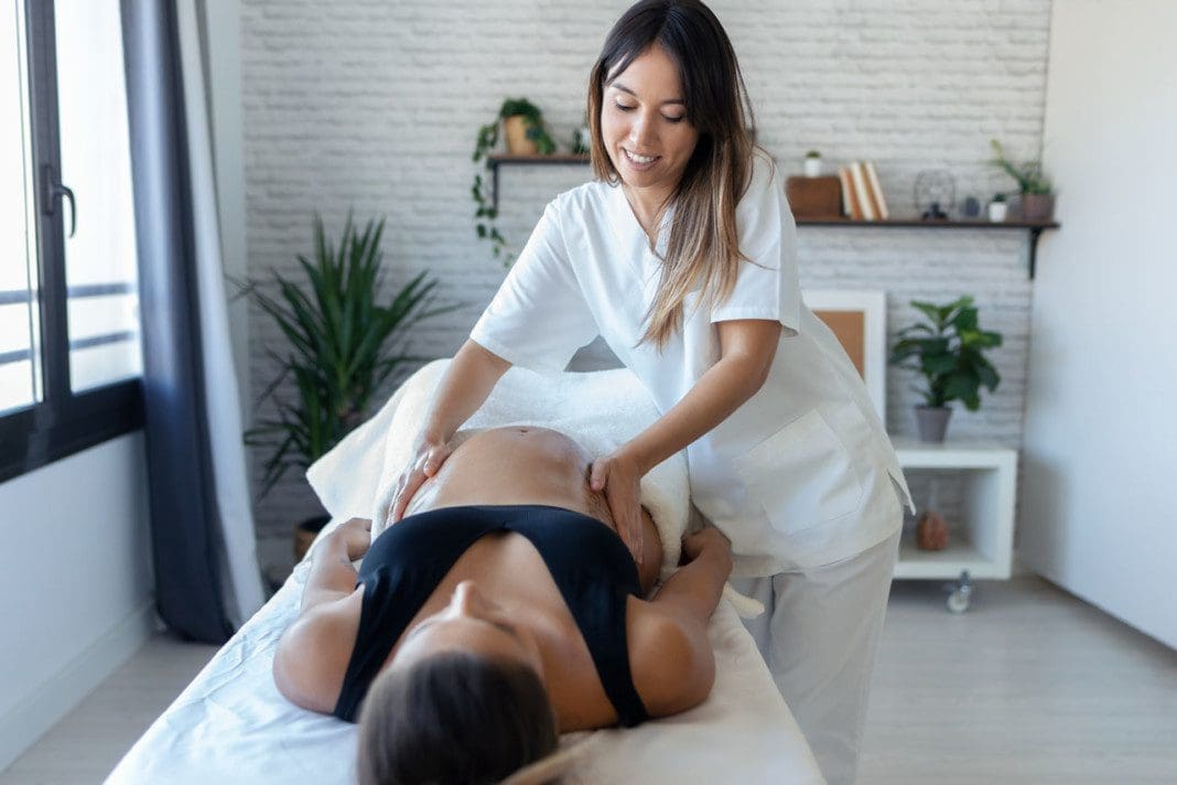 Beautiful young physiotherapist woman massaging tummy on pregnan