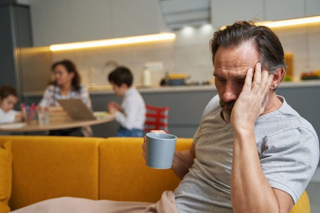 Male with headache sitting with tea on couch