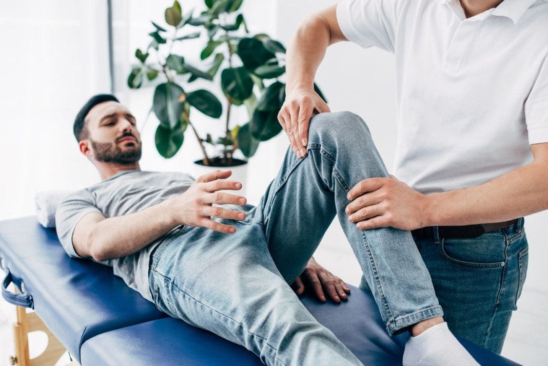 Physiotherapist massaging leg of patient lying on Massage Table