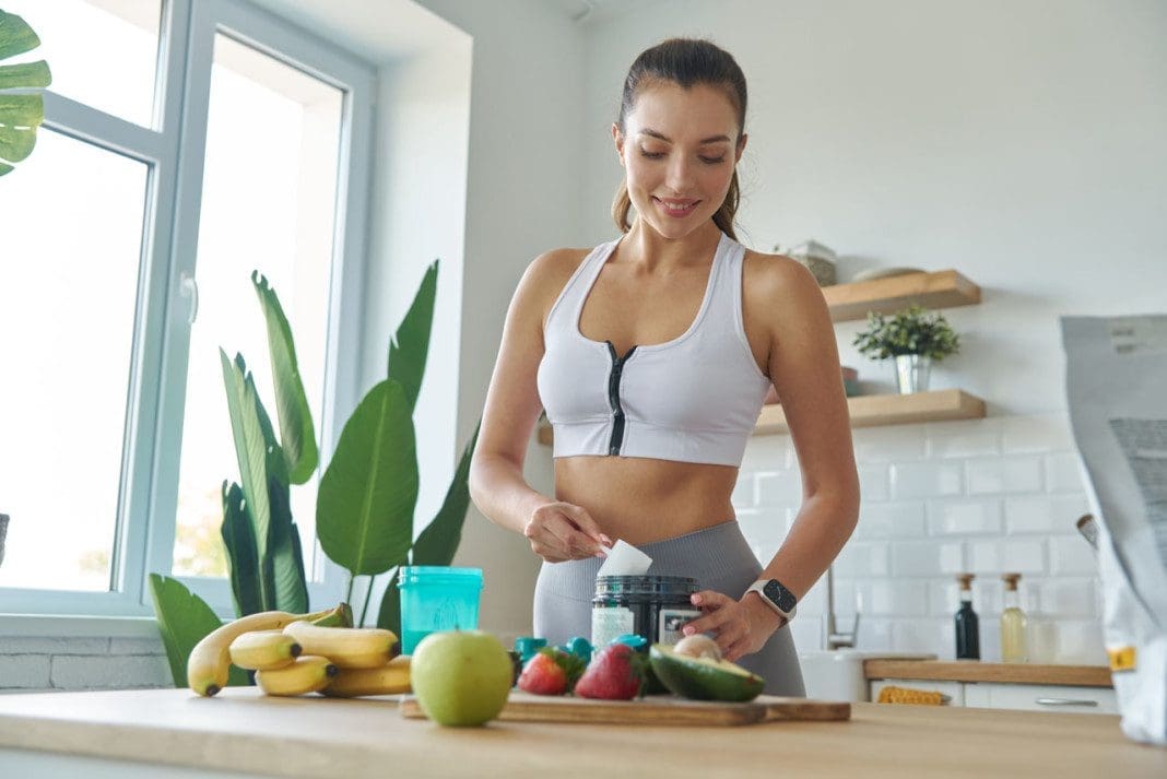 Happy young woman in sports clothing preparing protein cocktail