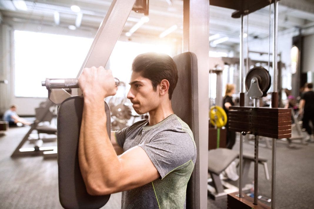 Hispanic man in gym sitting on bench, working out with weights
