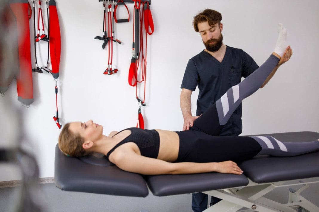Chiropractor stretches a female patient leg. Male physiotherapist is helping woman stretching his leg in exercise room