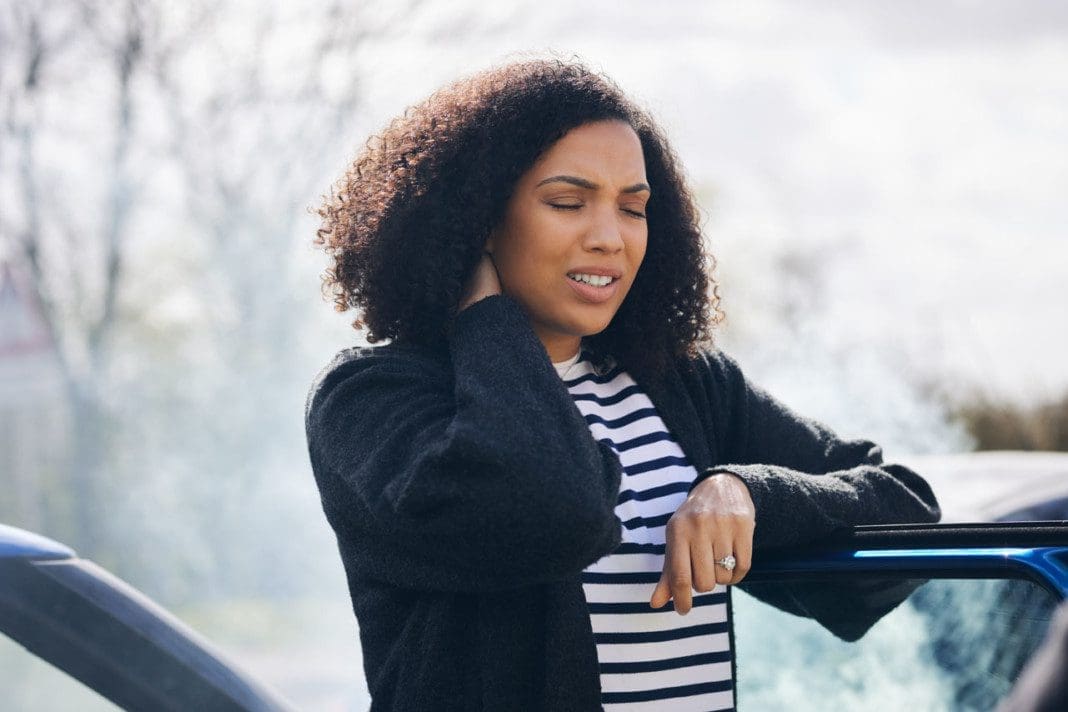 Female Driver With Whiplash Injury Standing By Damaged Car After