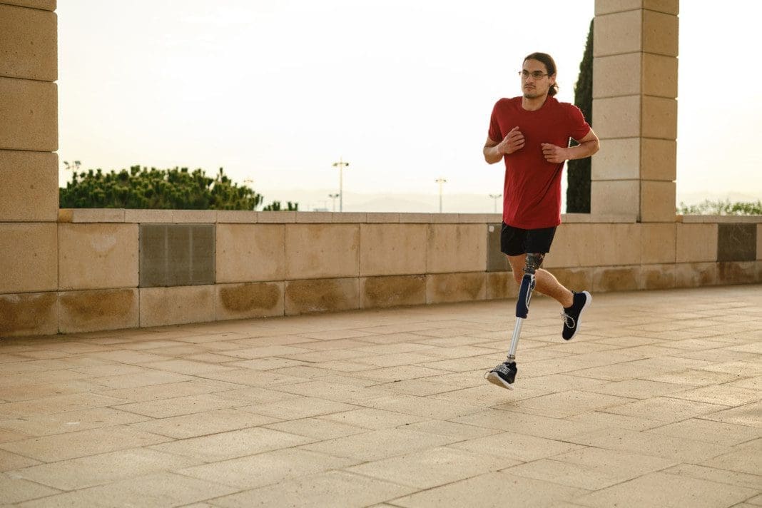 Young male runner with a prosthetic leg running outdoors.