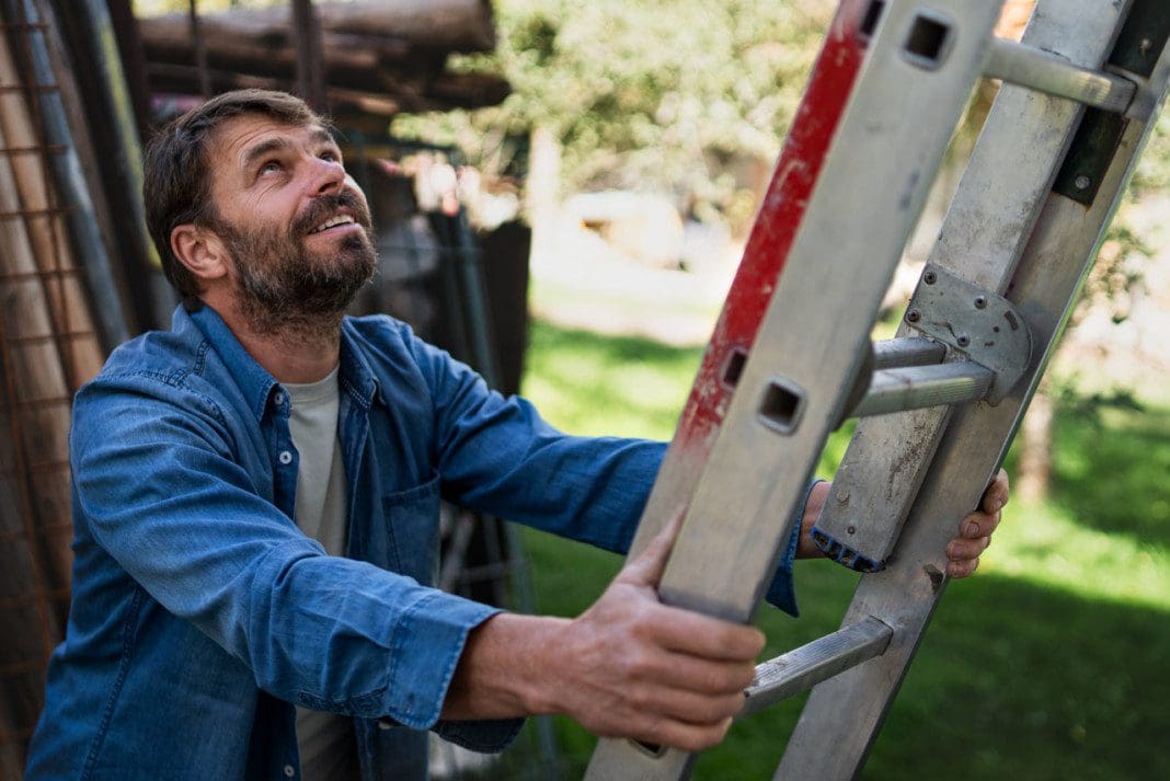 Side view of mature man climbing up the ladder.