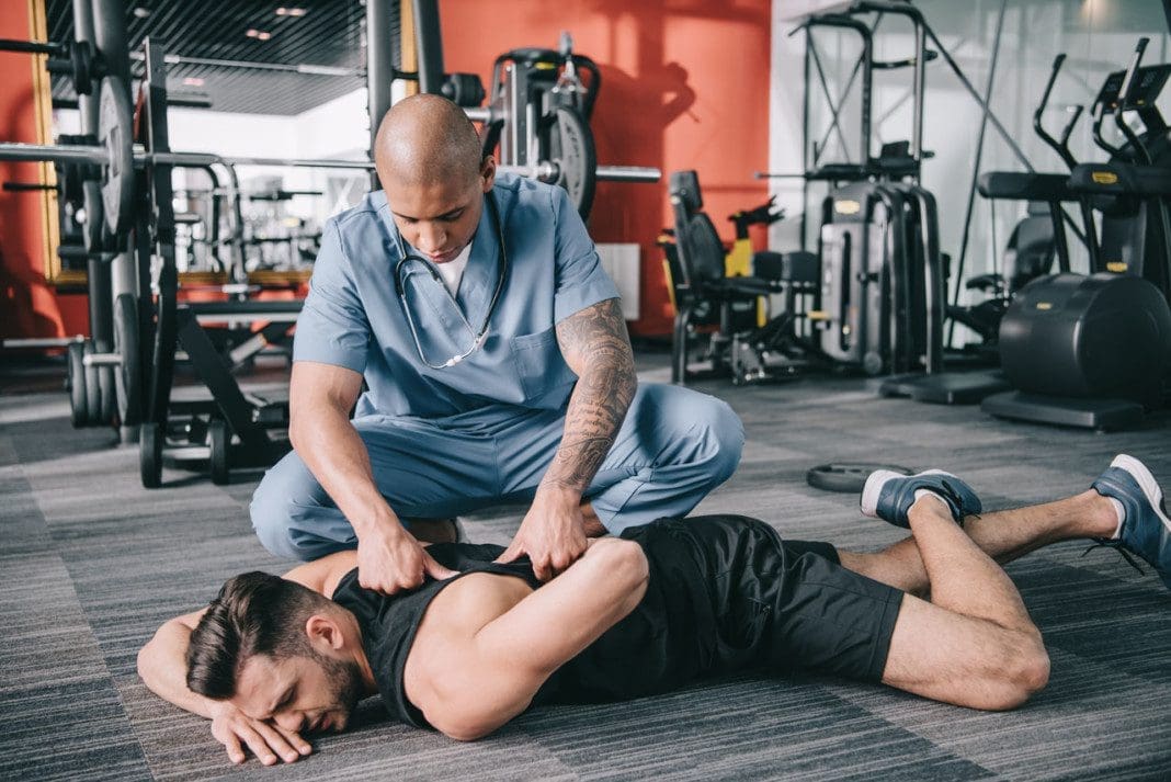 attentive american doctor examining injured back of sportsman ly