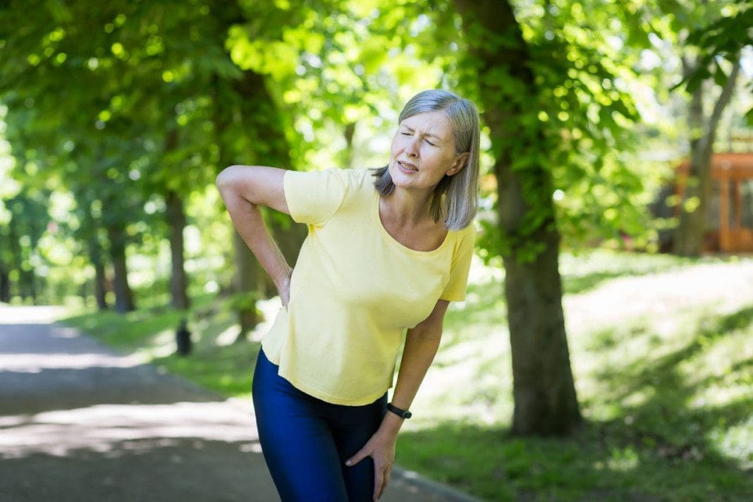 Senior active woman on a walk in the park injured her back, pensioner on a jog on a summer day