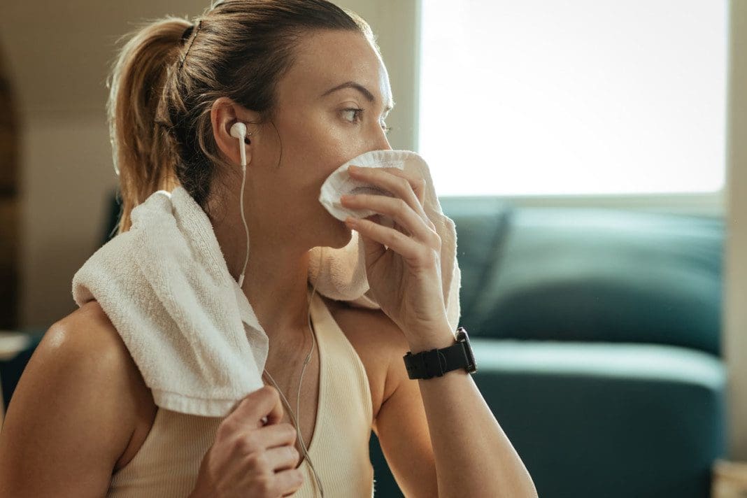 Pensive female athlete cleaning sweat with a towel after sports training.