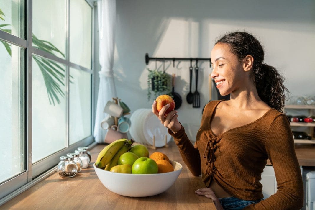 Young attractive Latino woman eat fruits on table in kitchen at