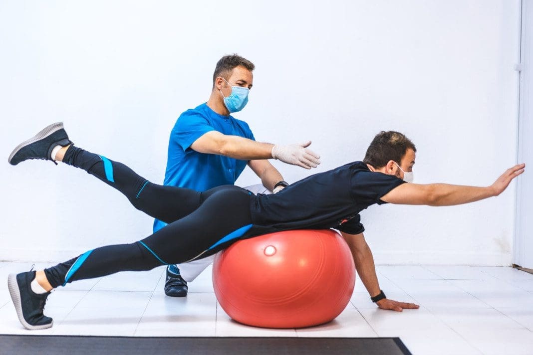 Physiotherapist with mask and a patient doing stretches upside down with rubber bands