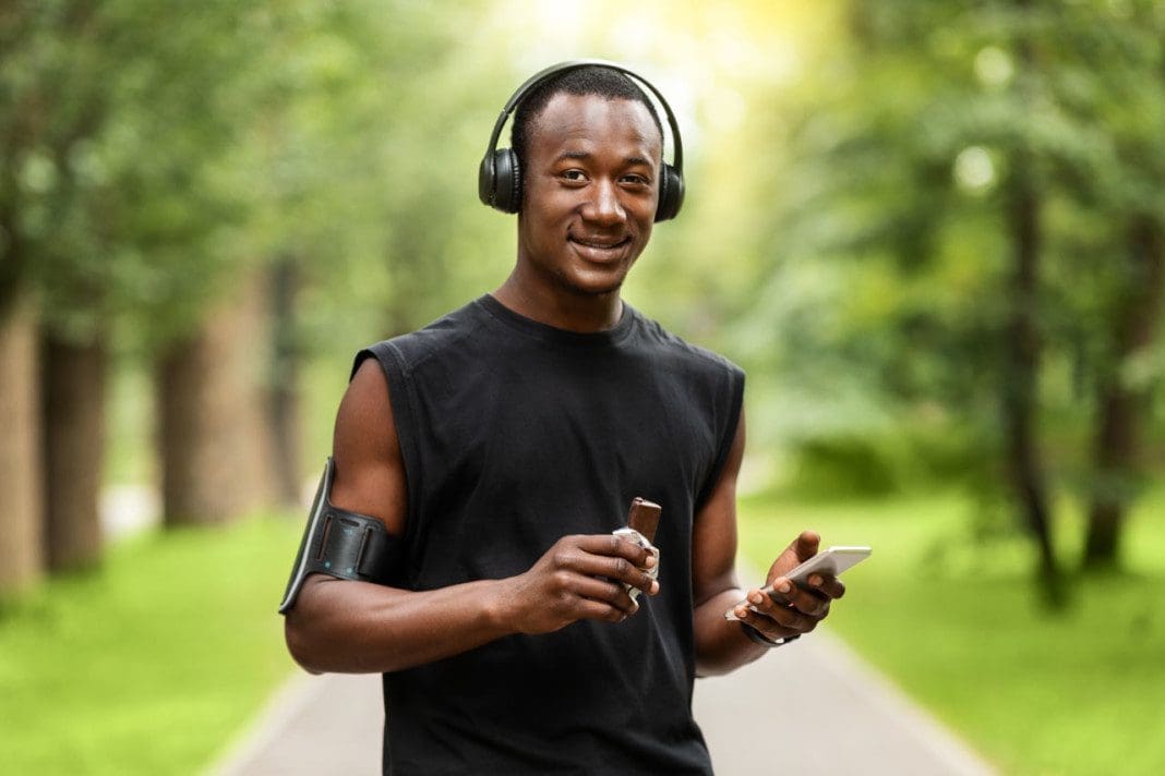 Smiling black guy sportsman eating protein bar while having break