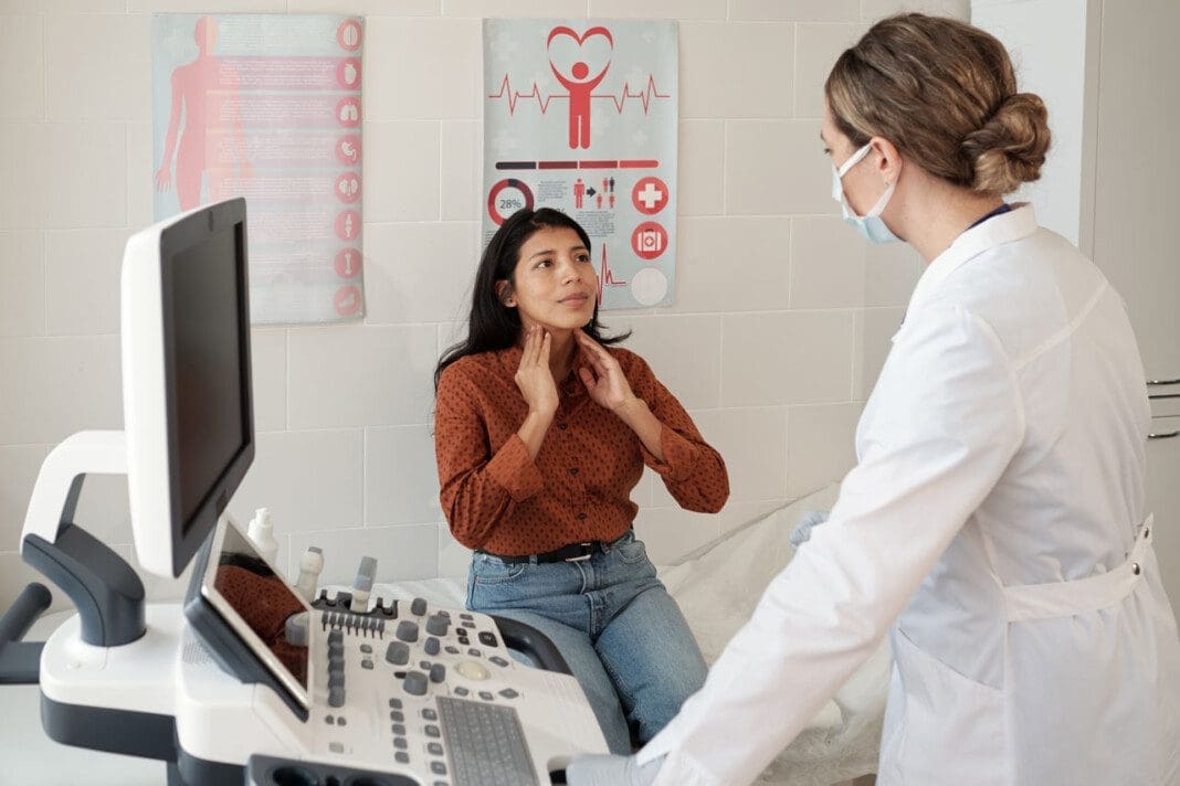 Young Hispanic female patient touching her thyroid in front of clinician