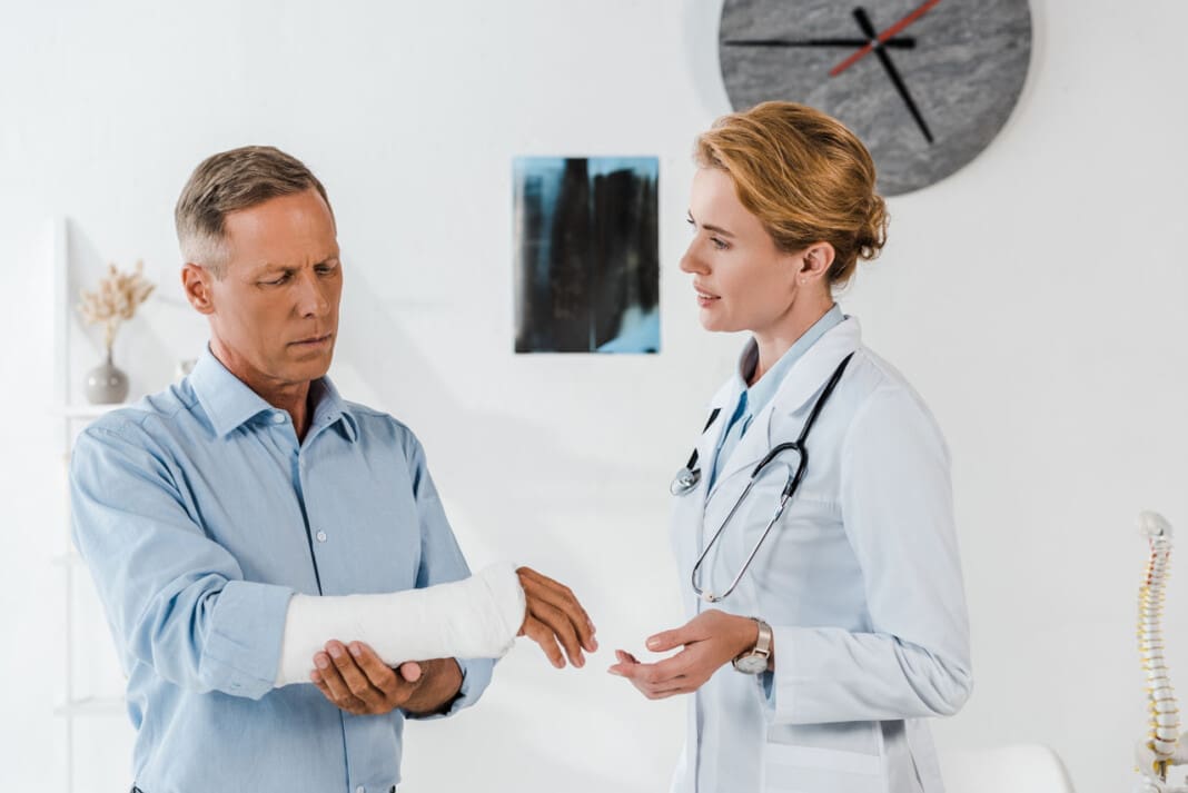attractive doctor looking at handsome man with broken arm