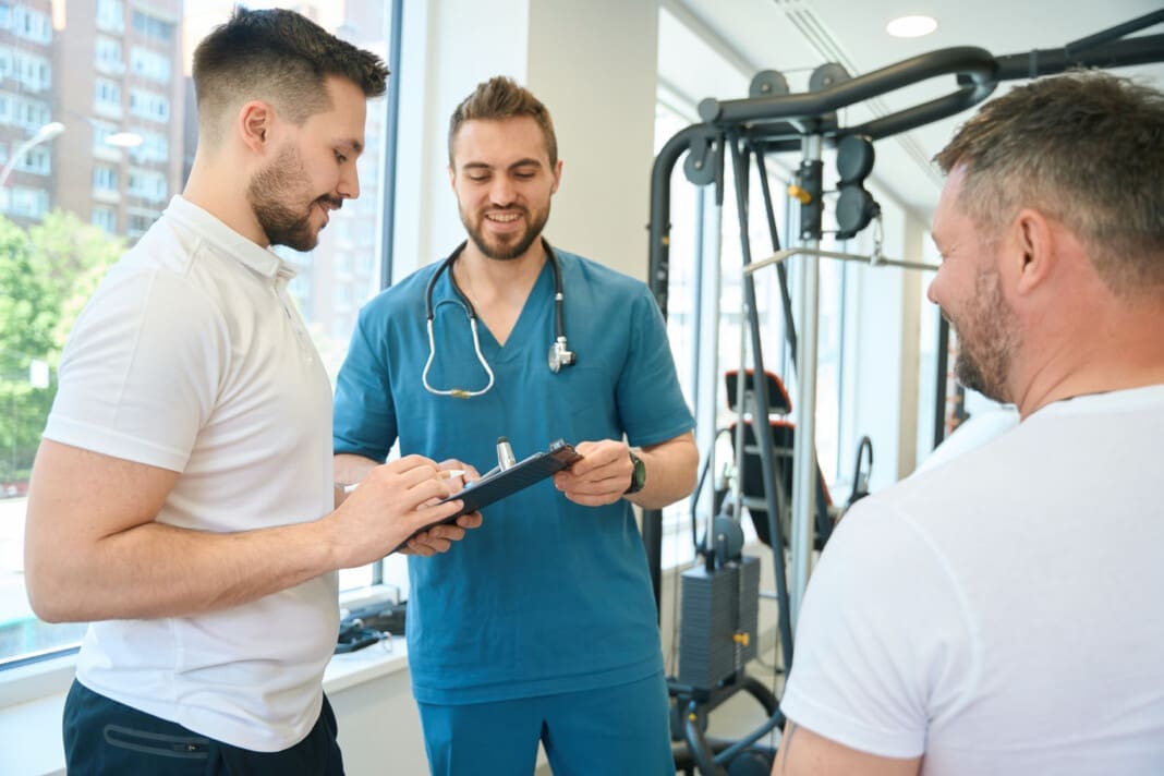 Physician and gym trainer discussing patient physical rehabilitation strategy