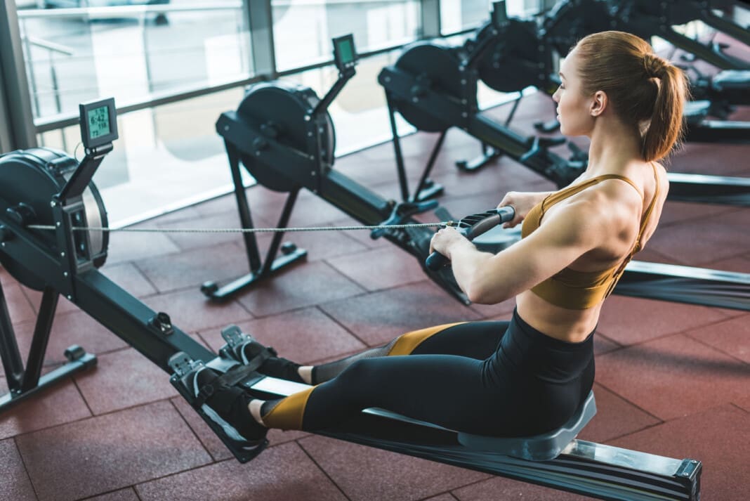 Young sportswoman doing exercise on rowing machine in sports cen