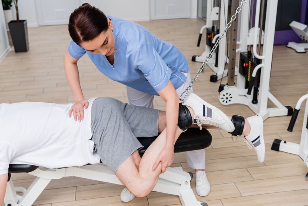 brunette physiotherapist stretching leg of man training in rehab