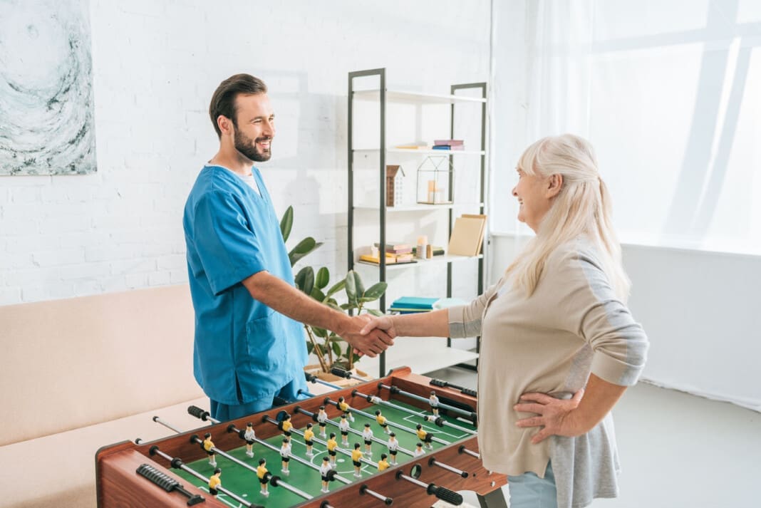 high angle view of smiling senior woman and caregiver shaking ha