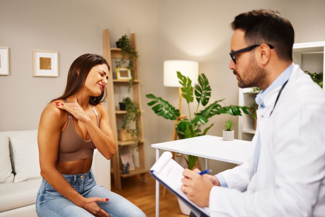 Young woman with shoulder pain is being examined by a physiatrist