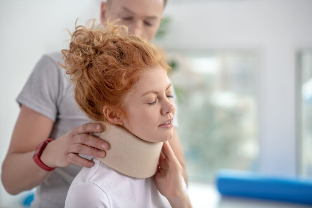Male physiotherapist examining neck fixator of female patient