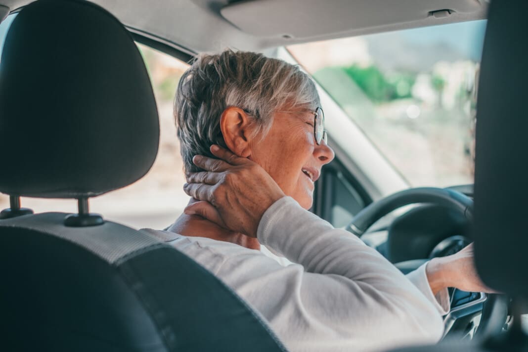 Rear view of old woman having neck pain while driving a car. One
